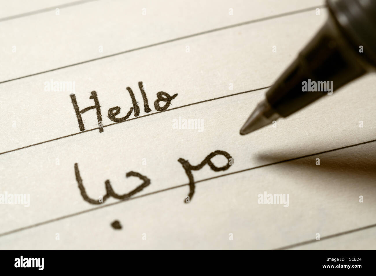 Beginner Arabic language learner writing Hello word in abjad Arabic alphabet on a notebook close-up shot Stock Photo