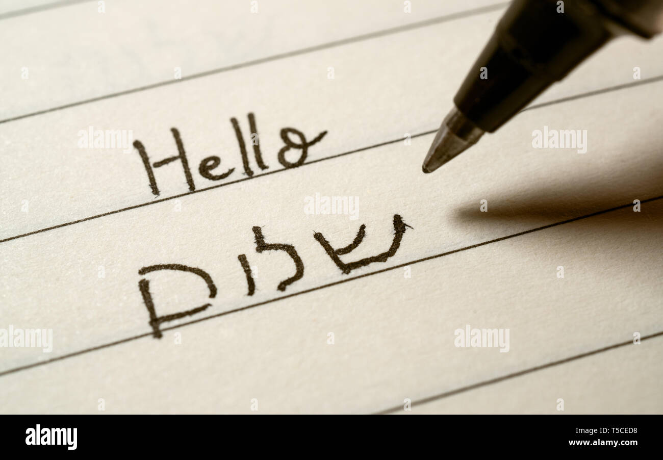 Beginner Hebrew language learner writing Hello shalom word in Hebrew alphabet on a notebook close-up shot Stock Photo