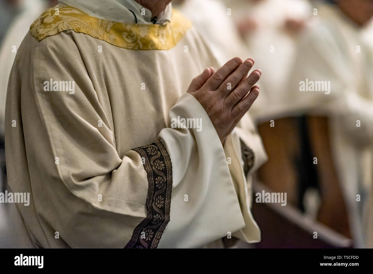 Priest with hands folded in prayer during Catholic mass. Stock Photo