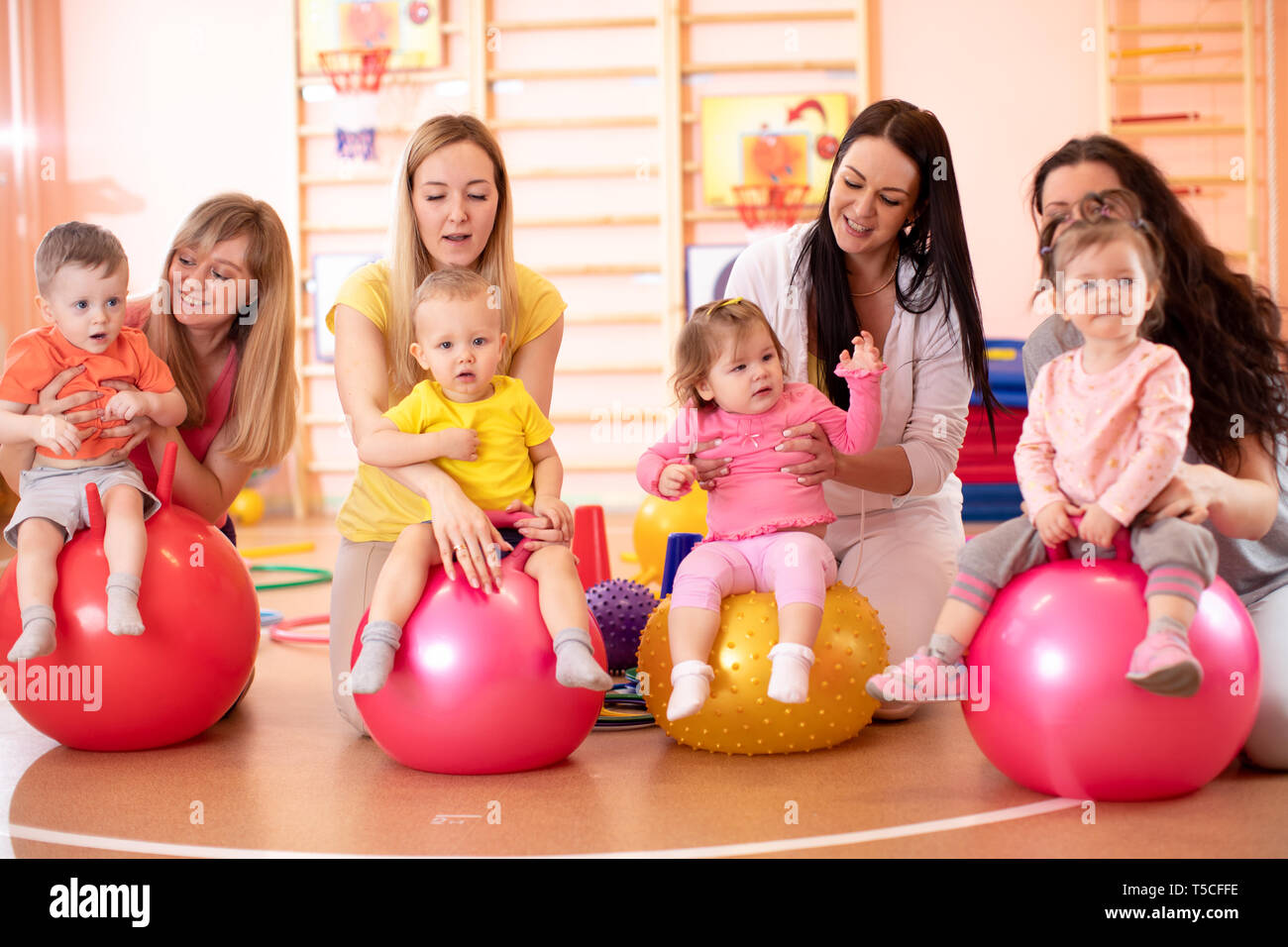 Group of young mothers and their babies doing yoga exercises on gymnastic balls at fitness gym Stock Photo