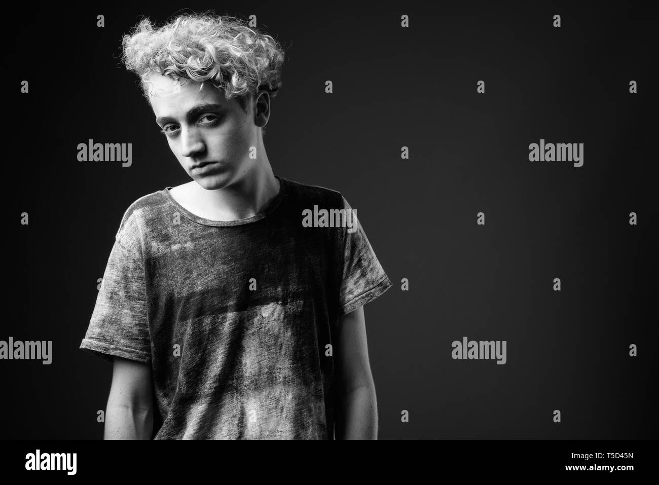 Skinny young man with curly hair against gray background in blac Stock Photo