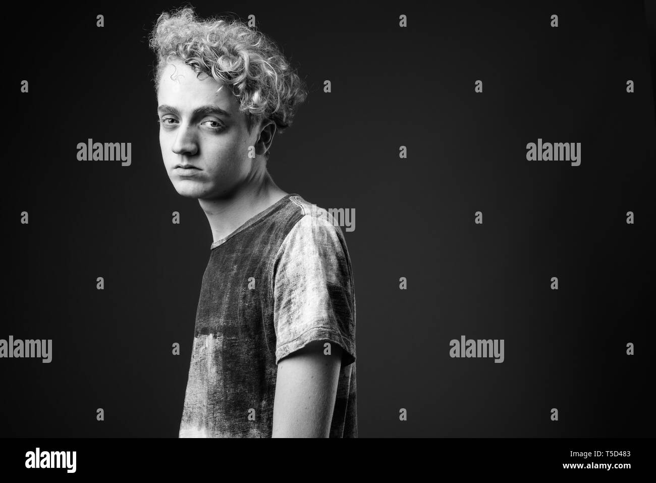 Skinny young man with curly hair against gray background in blac Stock Photo