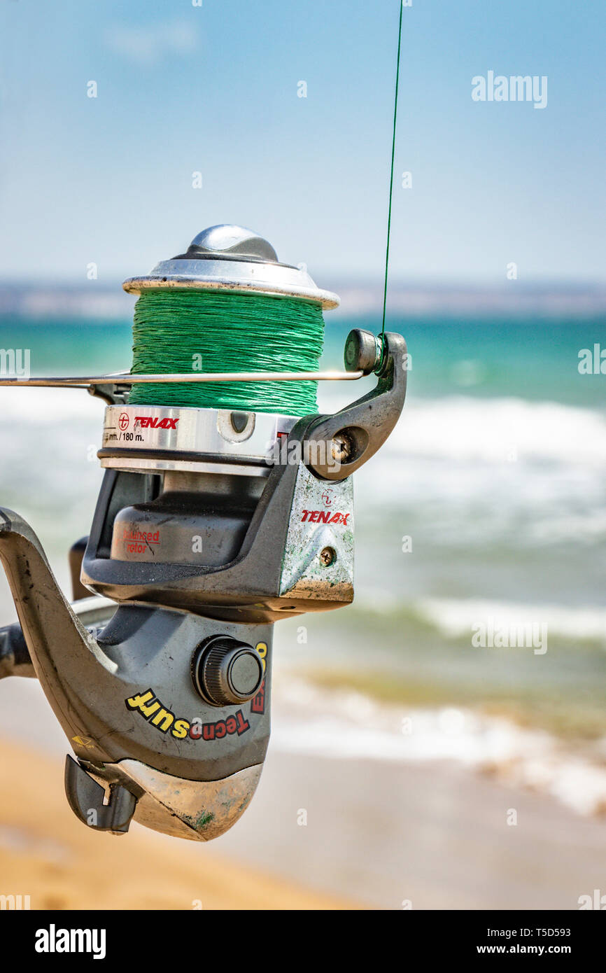 detail shot of Tenax surf fishing reel with blurred ocean background Stock Photo
