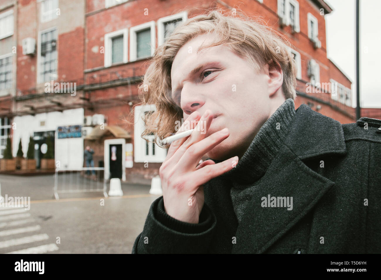 young blond guy smokes a cigarette in cold weather Stock Photo