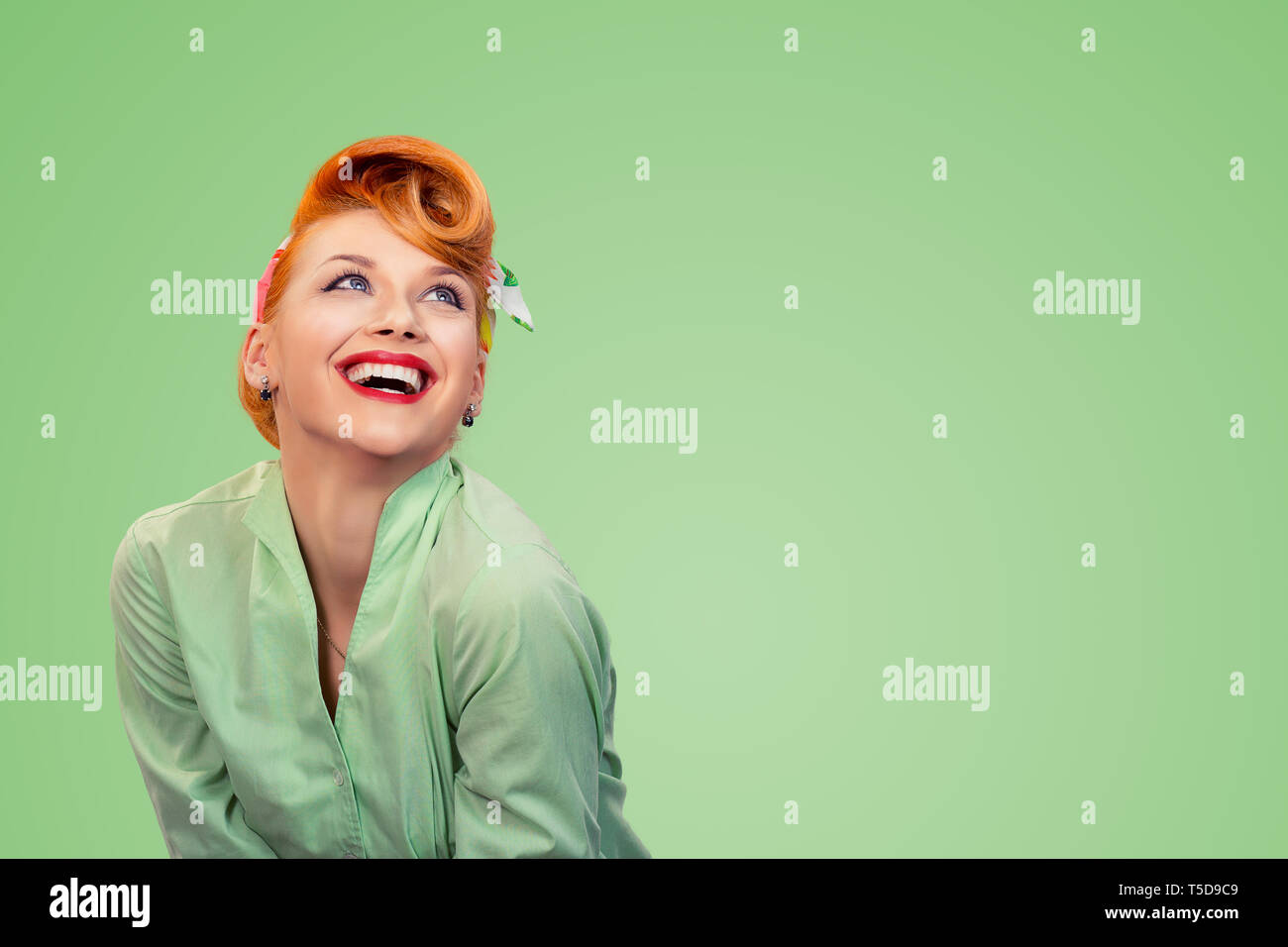 Closeup red head young excited woman pretty pinup girl green button shirt smiling laughing looking up isolated on yellow background retro vintage 50's Stock Photo