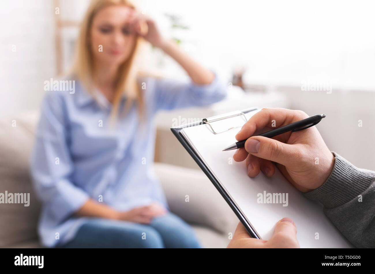 Depressed woman talking to psychotherapist, doctor taking notes Stock Photo
