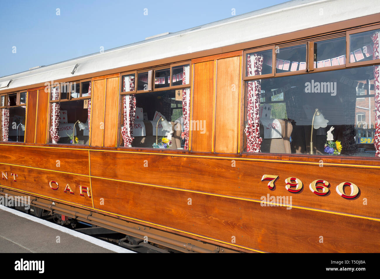 Exterior shot of varnished, teak, vintage railway dining carriage stationary alongside platform in the spring sunshine. SVR carriage for diners. Stock Photo