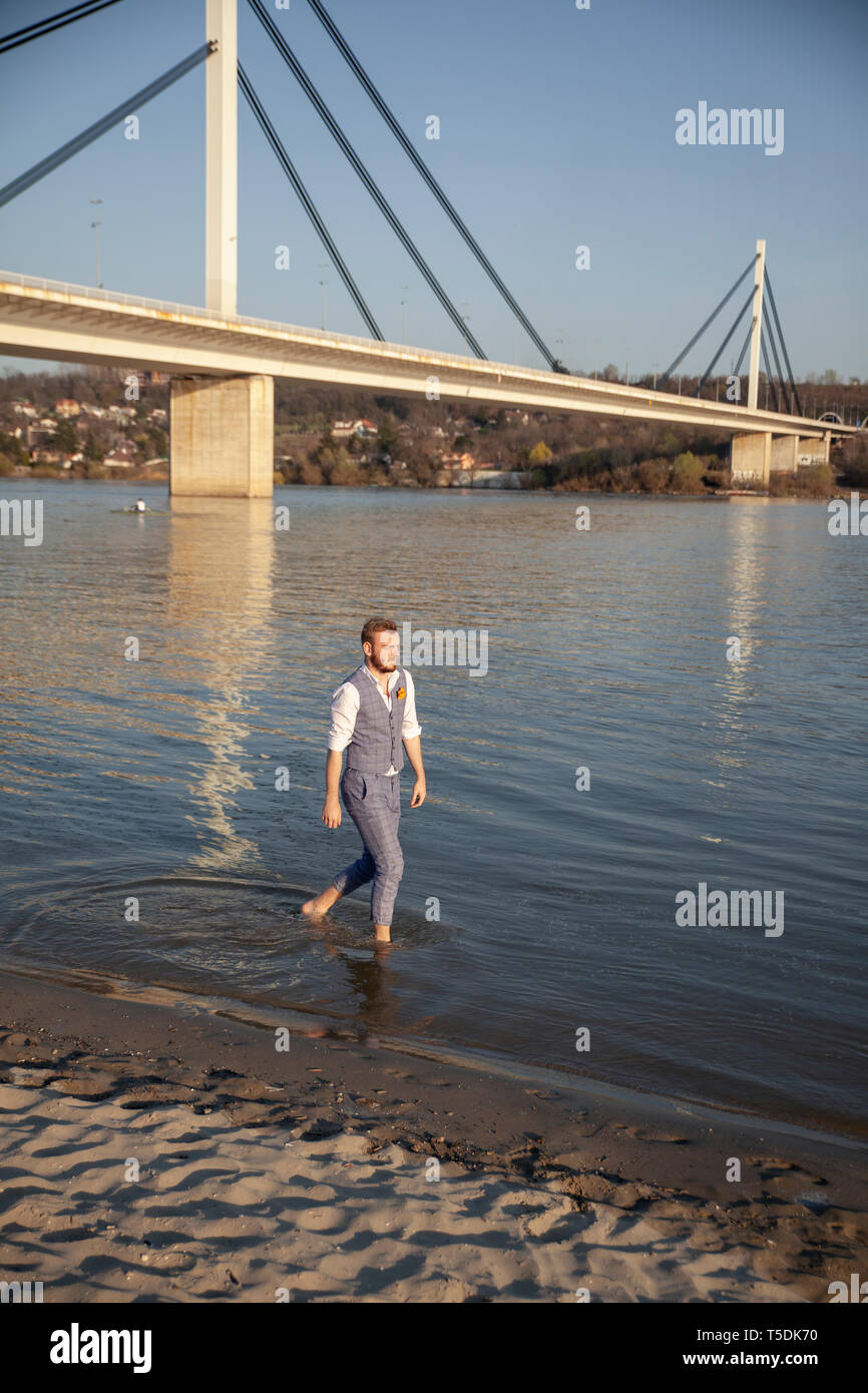 one young man, walking in river barefoot. Formal wear, wearing suit and ...