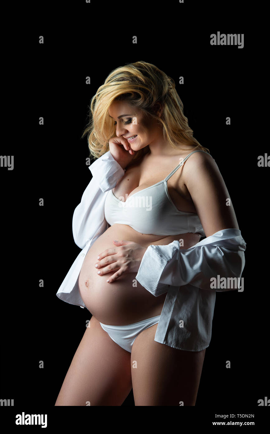 Beautiful smiling blonde pregnant woman in white clothes on a black background