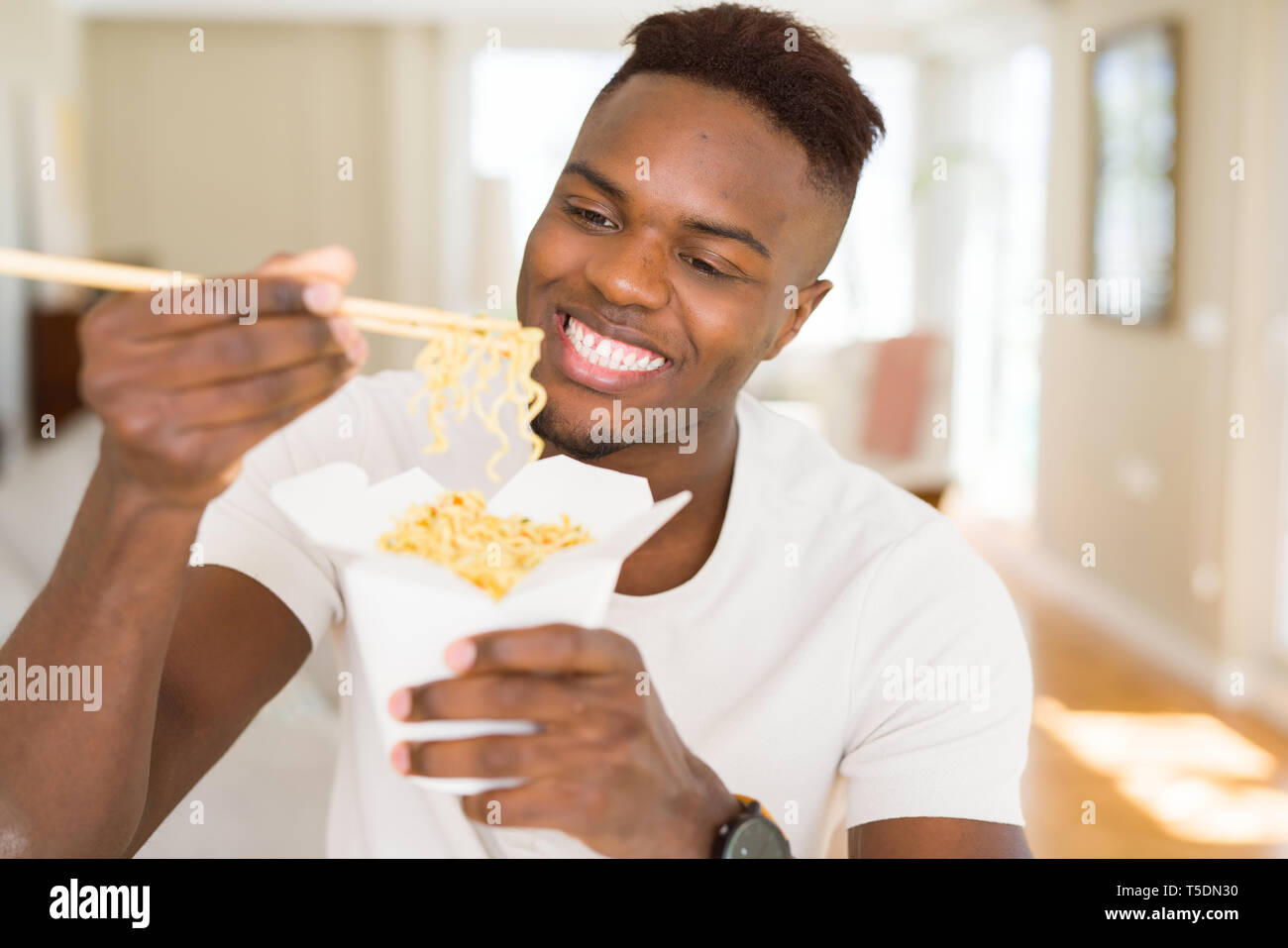 Handsome african man eating asian noodles in a delivery box, smiling