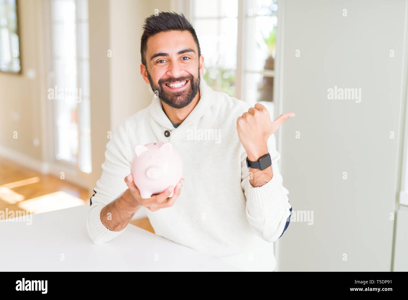Handsome hispanic man holding piggy bank pointing and showing with ...