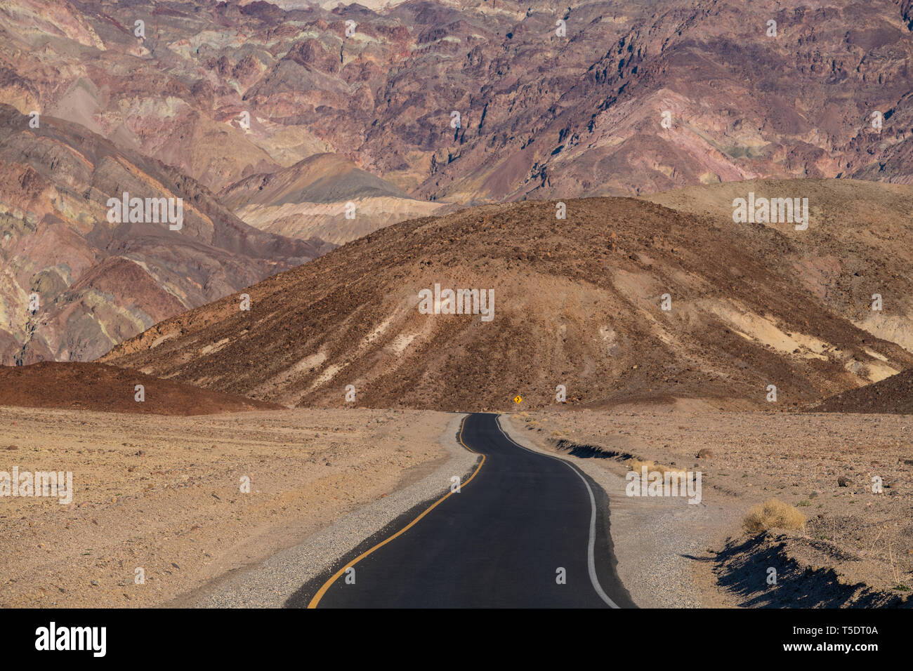 A highway in a barren desert landscape pointed towards a high wall of colorful mountains Stock Photo