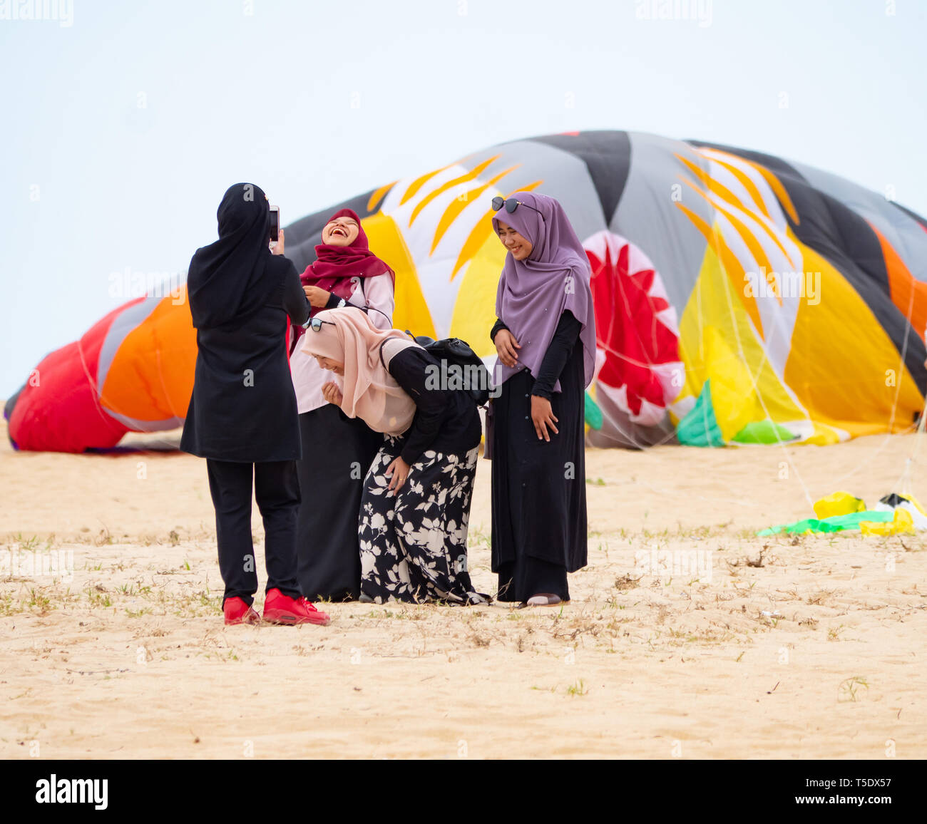 Four Muslim women wearing hijab taking photos on the beach in the conservative Kelantan State of Malaysia. In the background is a large deflated kite. Stock Photo