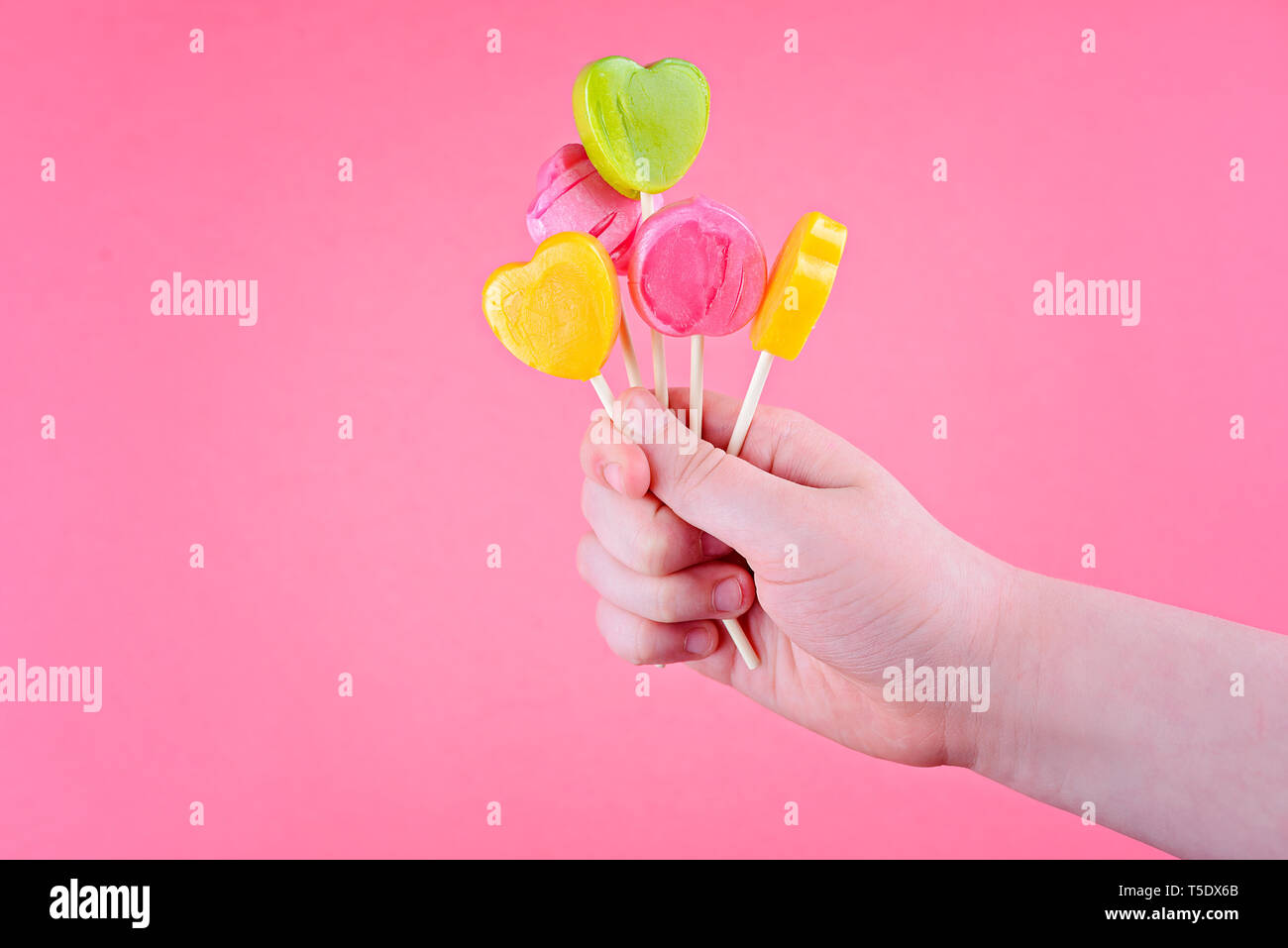 Lollipops of yellow, pink, green colors on wooden stick in the shape of circle, heart, flower. In the children's hand. Stock Photo