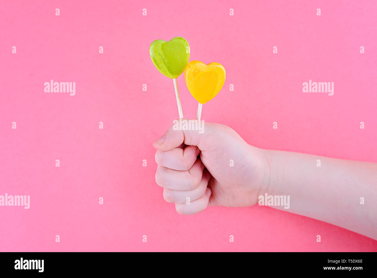 Yellow and Green Heart Shaped Lollipops. In the children's hand. On pink background Stock Photo