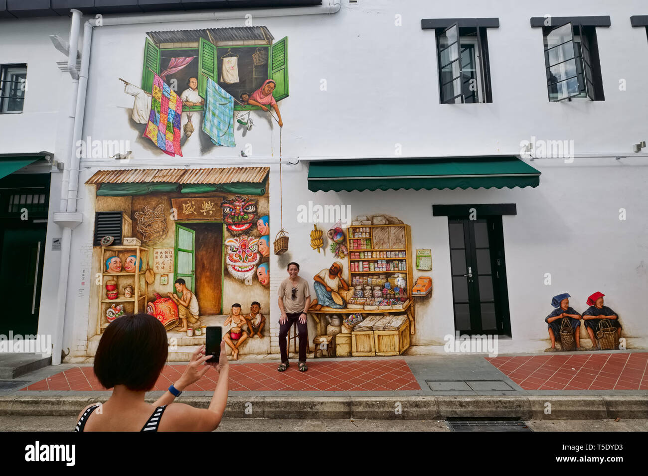 Tourists taking photos at a wall painting by Yip Yew Chong in Mohamed Ali Lane, Chinatown, Singapore, depicting local scenes of decades gone by Stock Photo