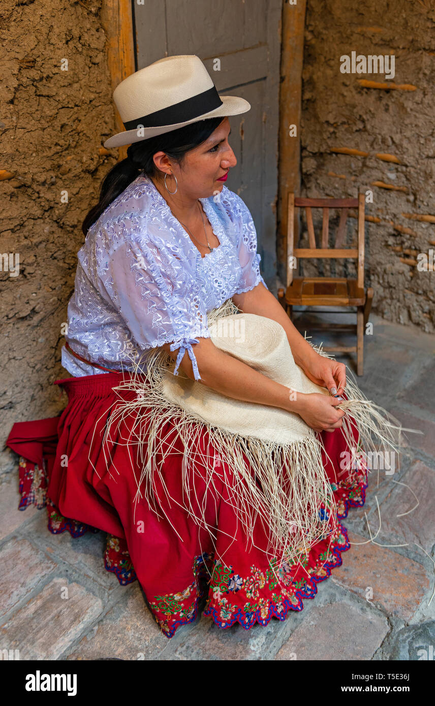Indigenous Chola Cuencana woman in traditional clothing showing the weaving technique of Panama hat, Unesco Intangible heritage of Cuenca, Ecuador. Stock Photo