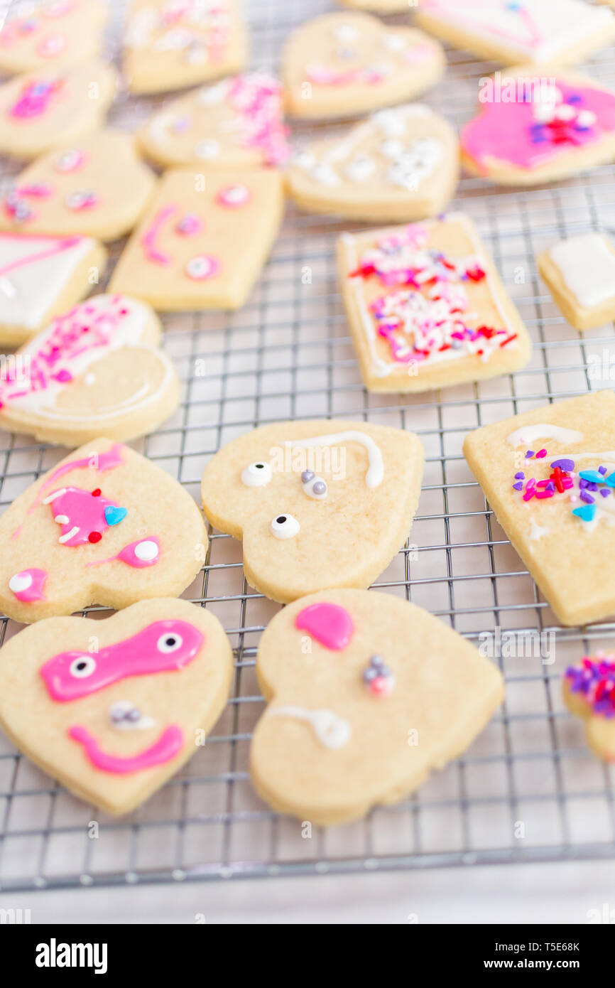 Decorating heart shape sugar cookies with royal icing and pink sprinkles for Valentine's day