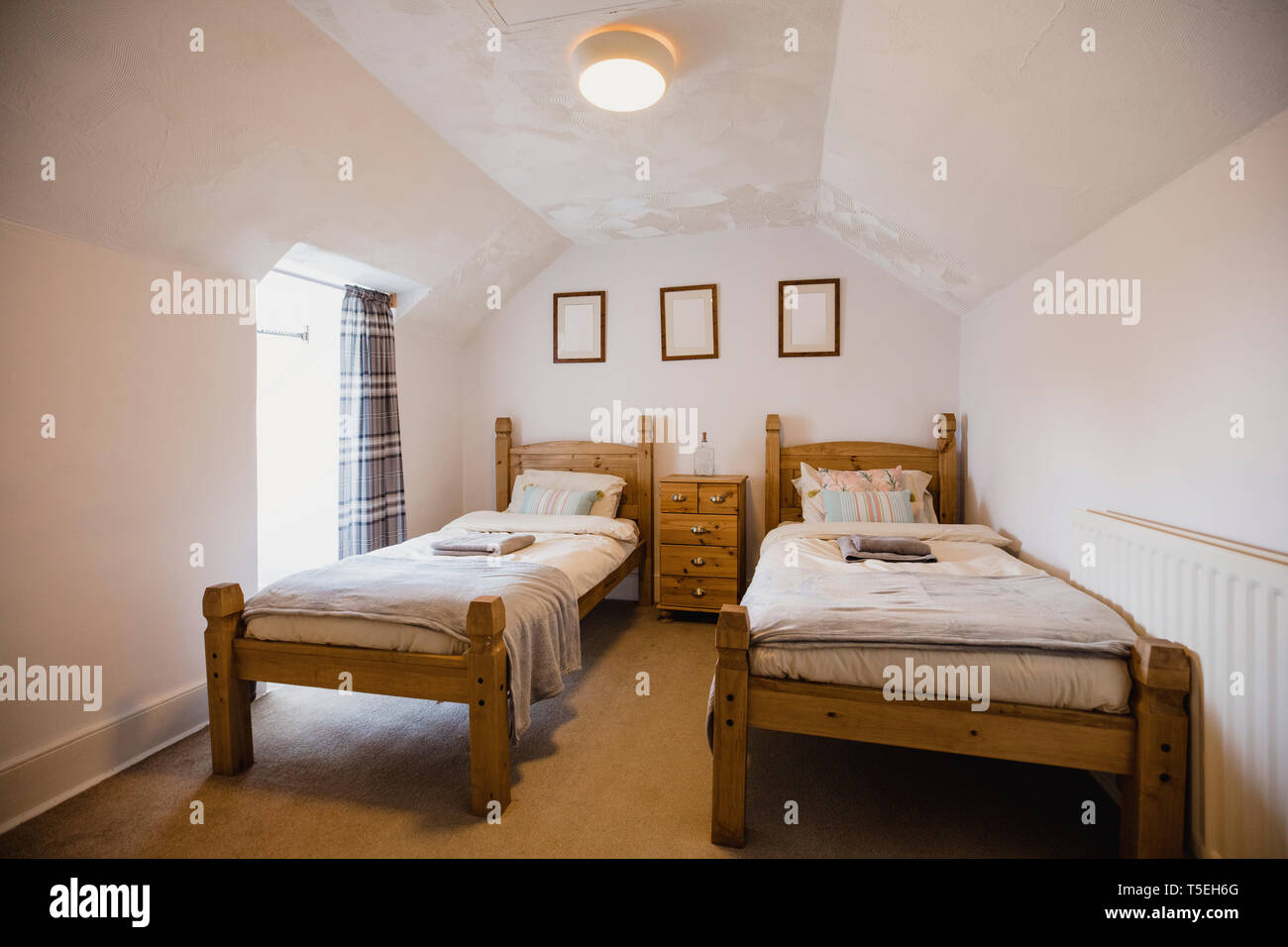 Interior shot of a empty bedroom. There are two single wooden beds against a wall with a set of drawers between them. Stock Photo
