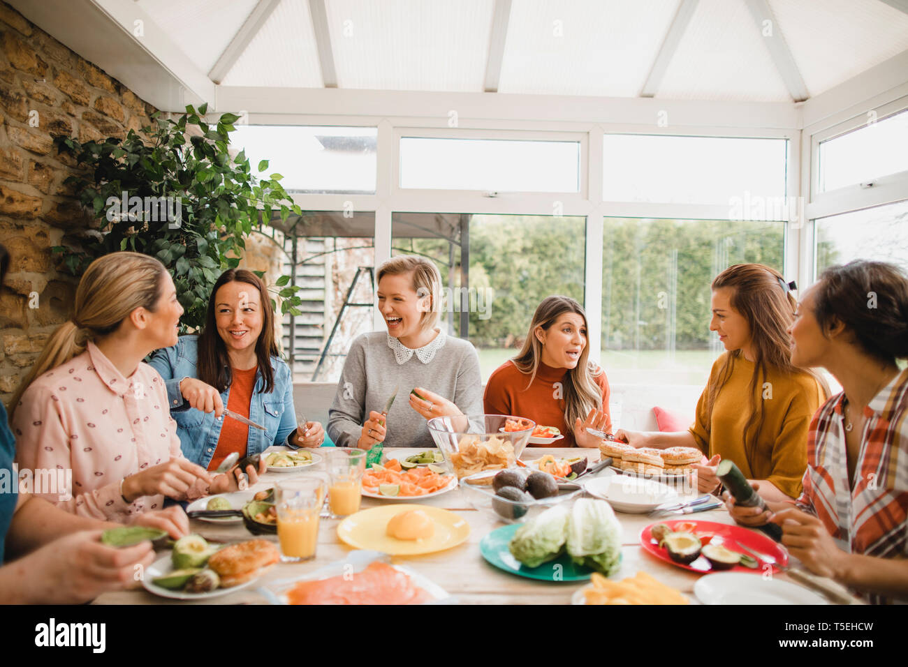 Small group of female friends preparing a healthy lunch inside of a conservatory on a weekend away. Stock Photo