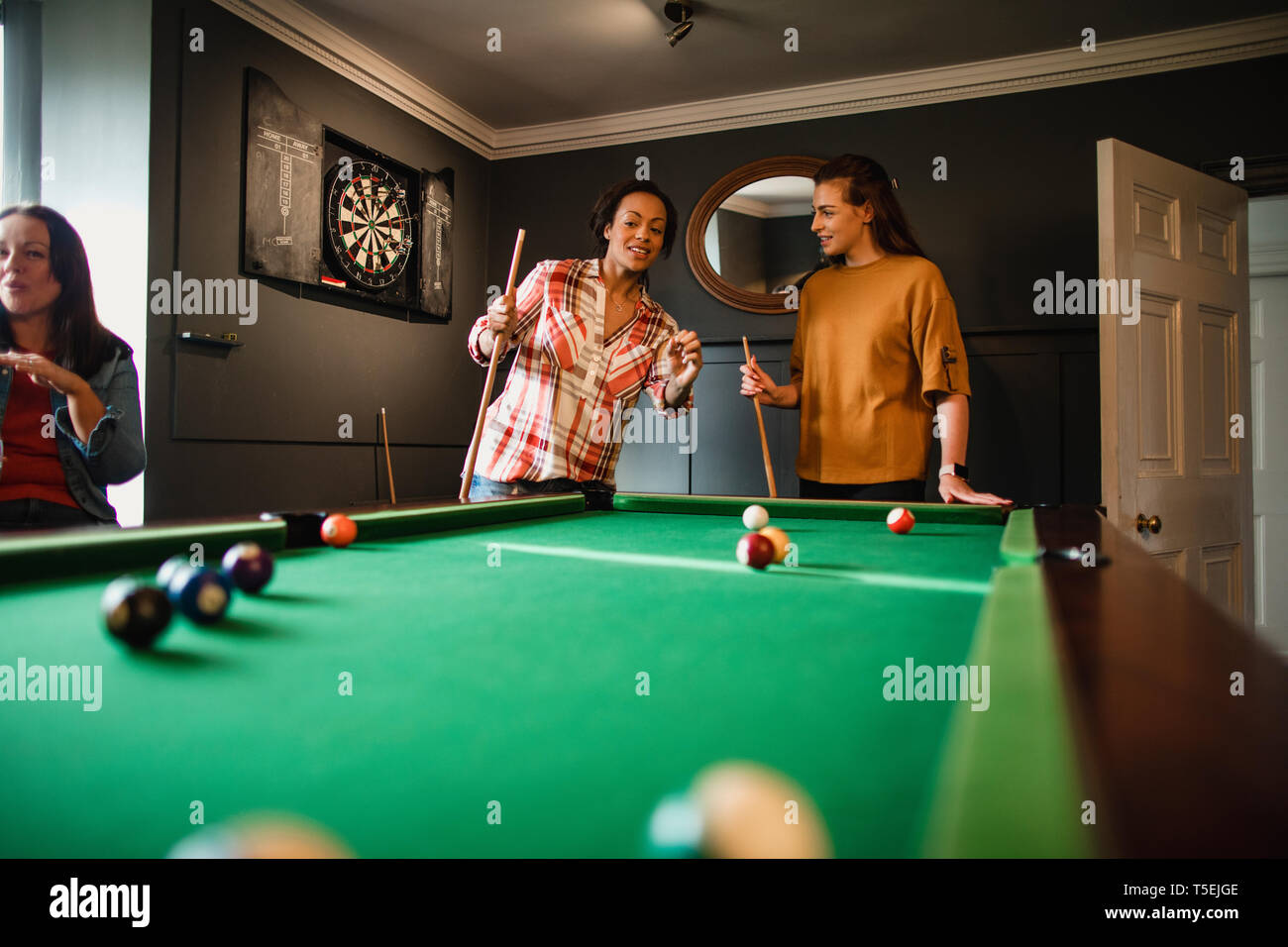 Small group of female friends playing a game of pool in a games room in a house. Stock Photo