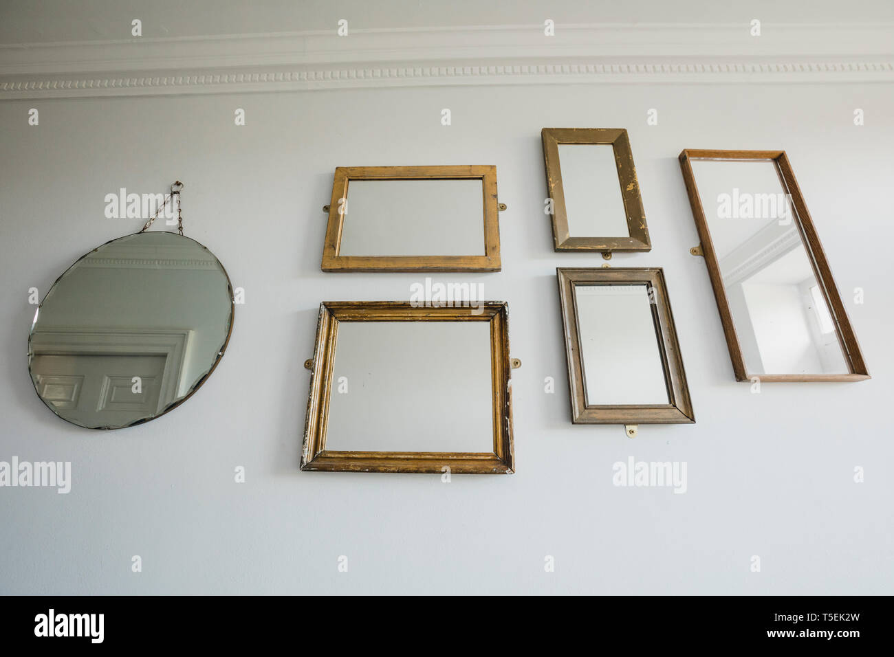 Low angle view of a wall in a house which has a variety of different shaped mirrors hanging on the wall. Stock Photo