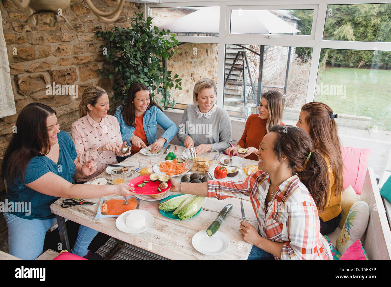 Small group of female friends with a mixed age range sitting at a table preparing their dinner. Stock Photo
