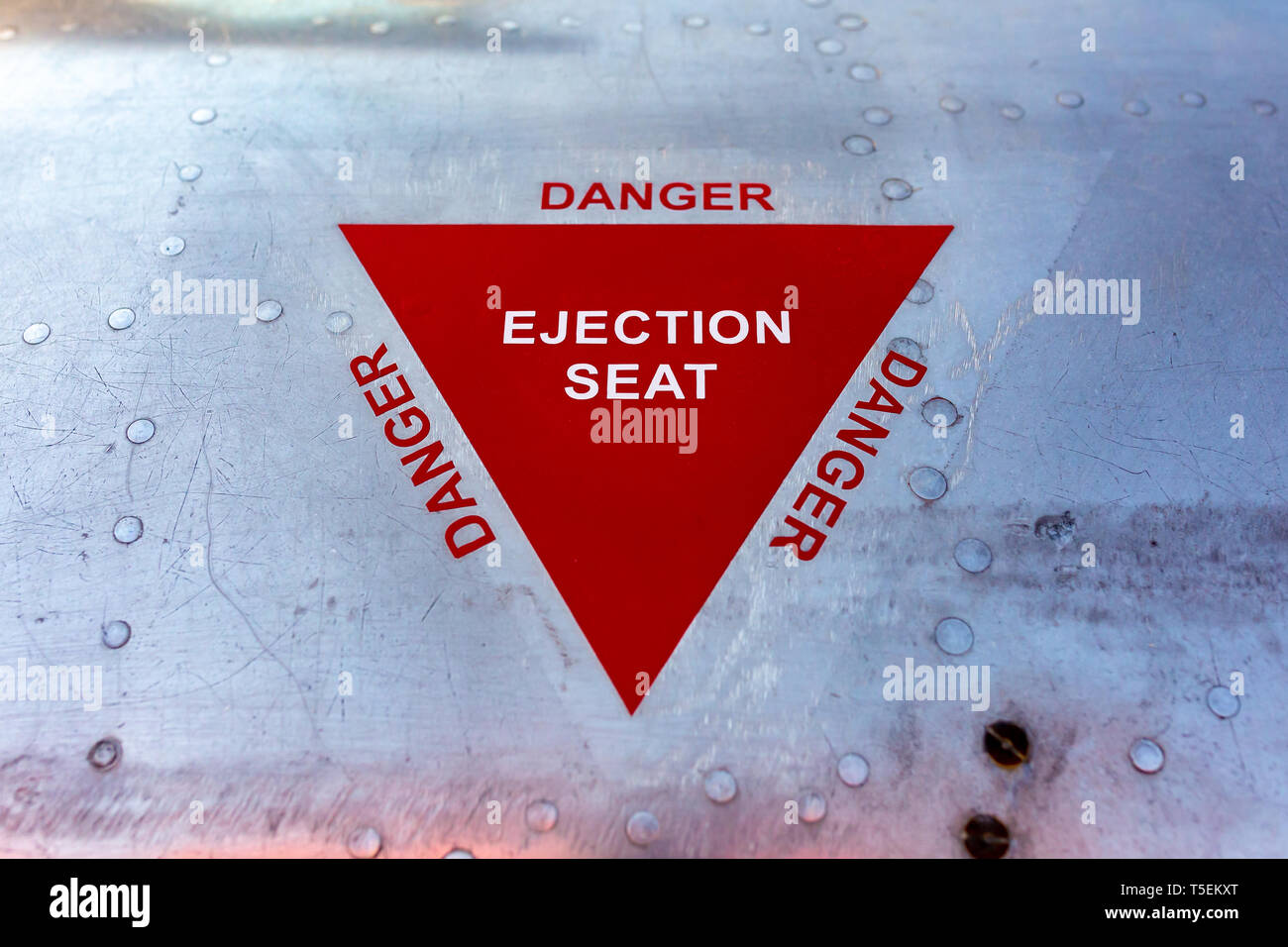 Close up colour photograph of military aviation warning of ejection seat printed on worn shiny aluminium shell. Stock Photo
