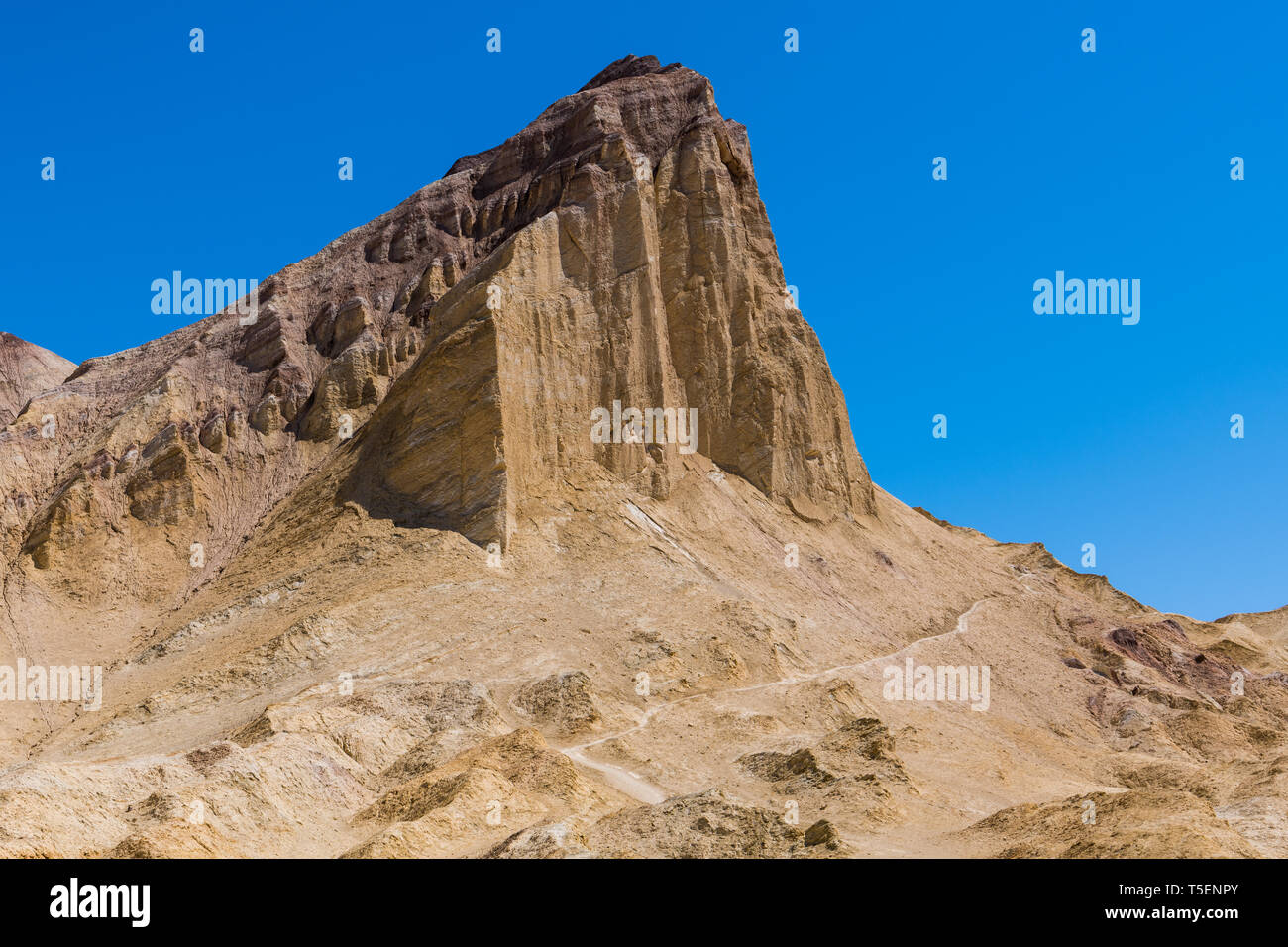 A hiking trail traverses the base of a high desert mountain peak in a vast colorful desert landscape -  Manly Beacon in Death Valley National Park Stock Photo