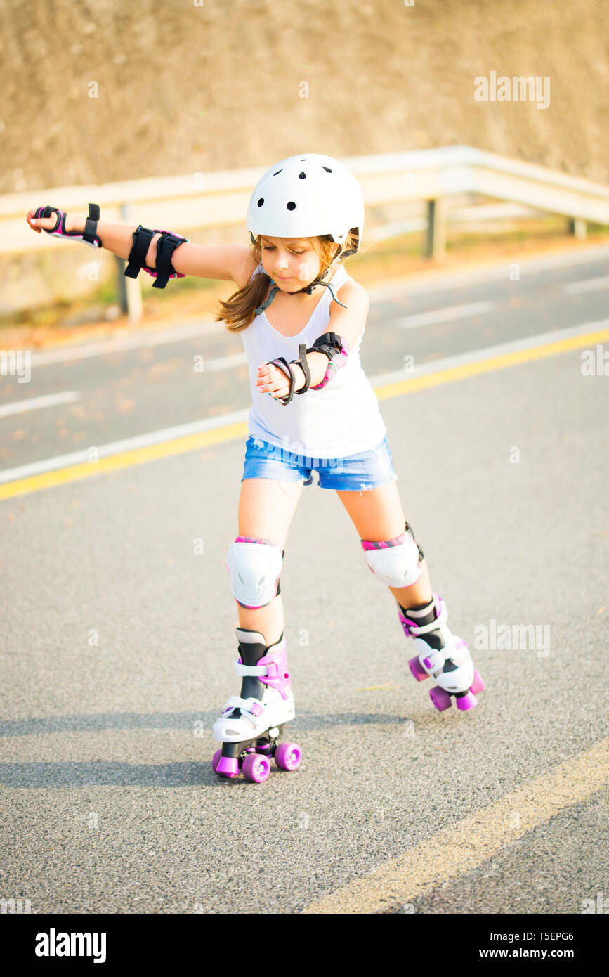 A little caucasian girl with roller quad rolling in the sun summer evening. Rollerblading and outdoor activity concept Stock Photo