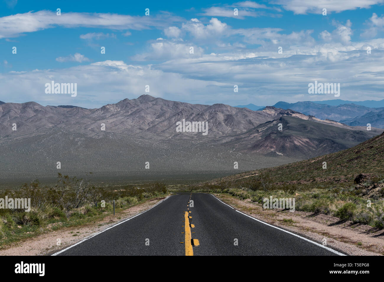 A highway moving towards perspective toward a mountain range in the desert landscape of Death Valley National Park Stock Photo