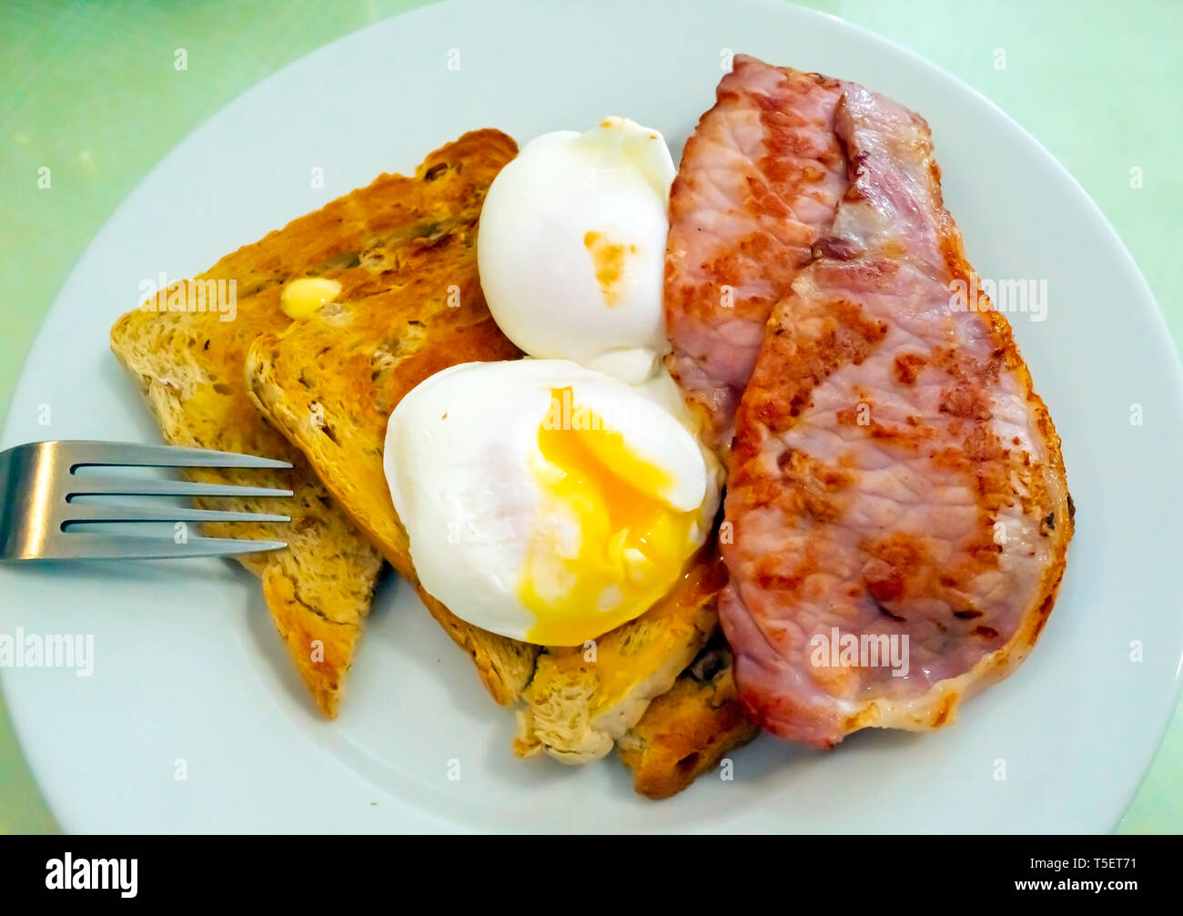 Breakfast snack in Yorkshire granary toast with two slices of fried bacon and two soft poached eggs one cut open Stock Photo