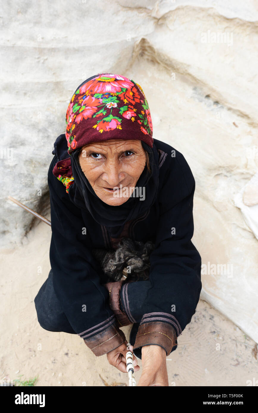 Old and weathered Bedouin woman spinning wool for weaving in Little Petra, Jordan. Stock Photo