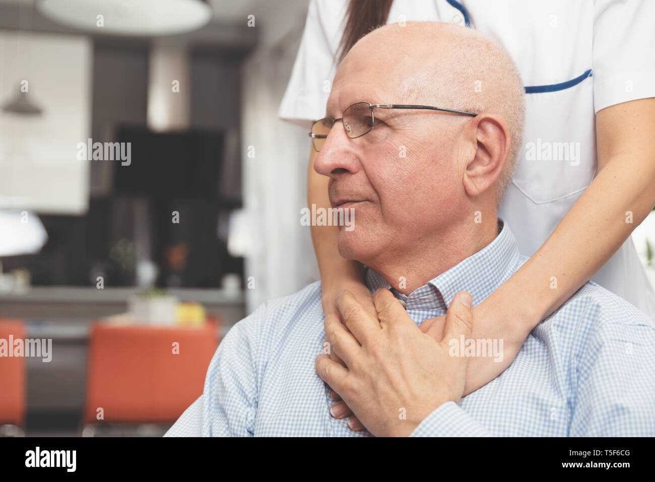 Health visitor and a senior man during home visit. Happy patient is holding caregiver for a hand while spending time together Stock Photo