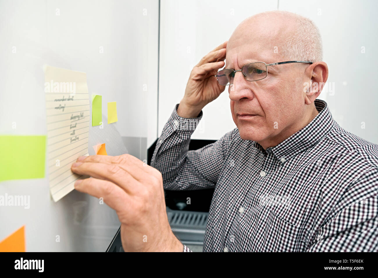 Elderly man looking at notes. Forgetful senior with dementia, memory problem, health concept Stock Photo