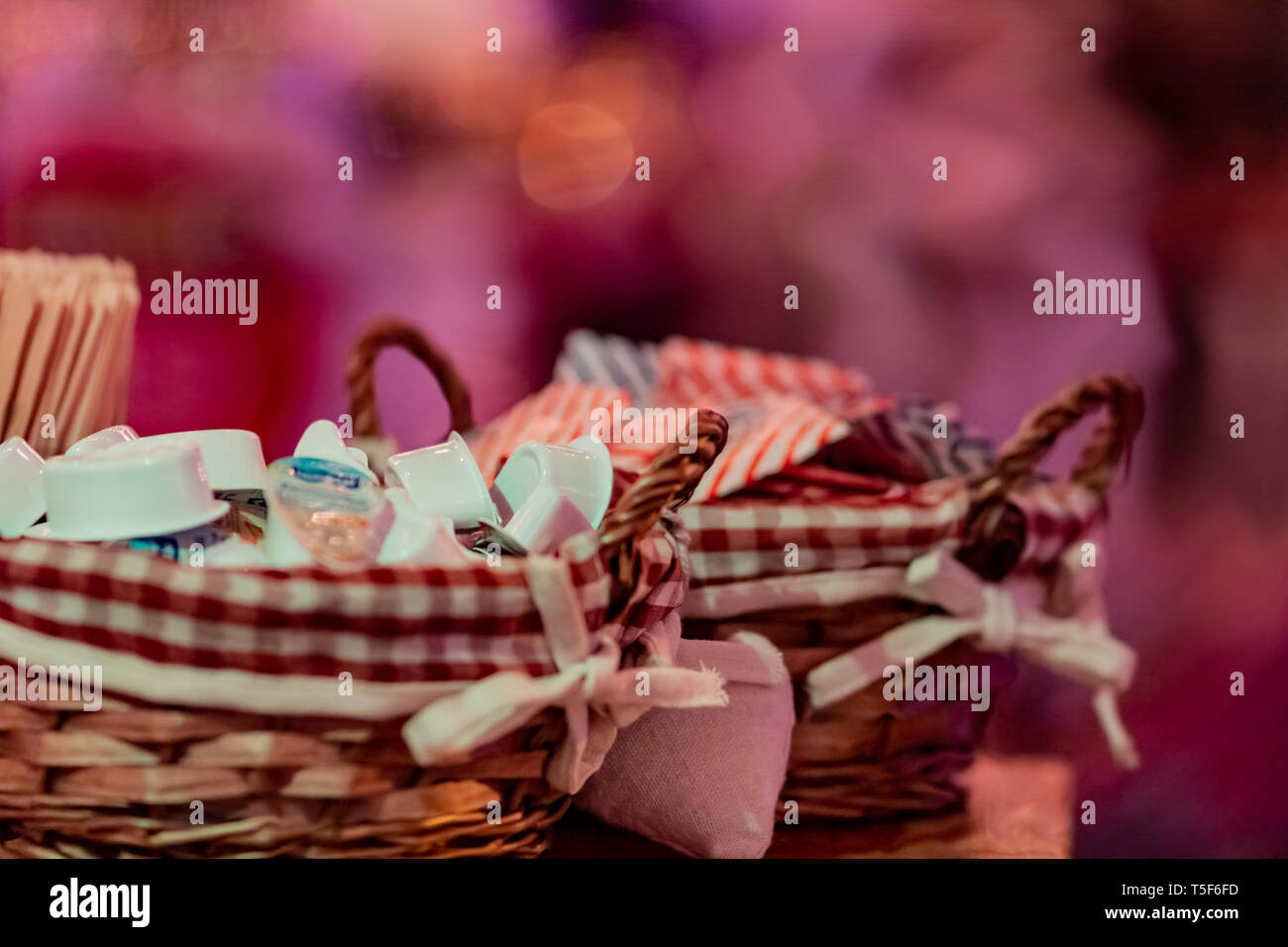 Small milk, coffee creamer pots in a basket on red blur background. Mono portions, for catering