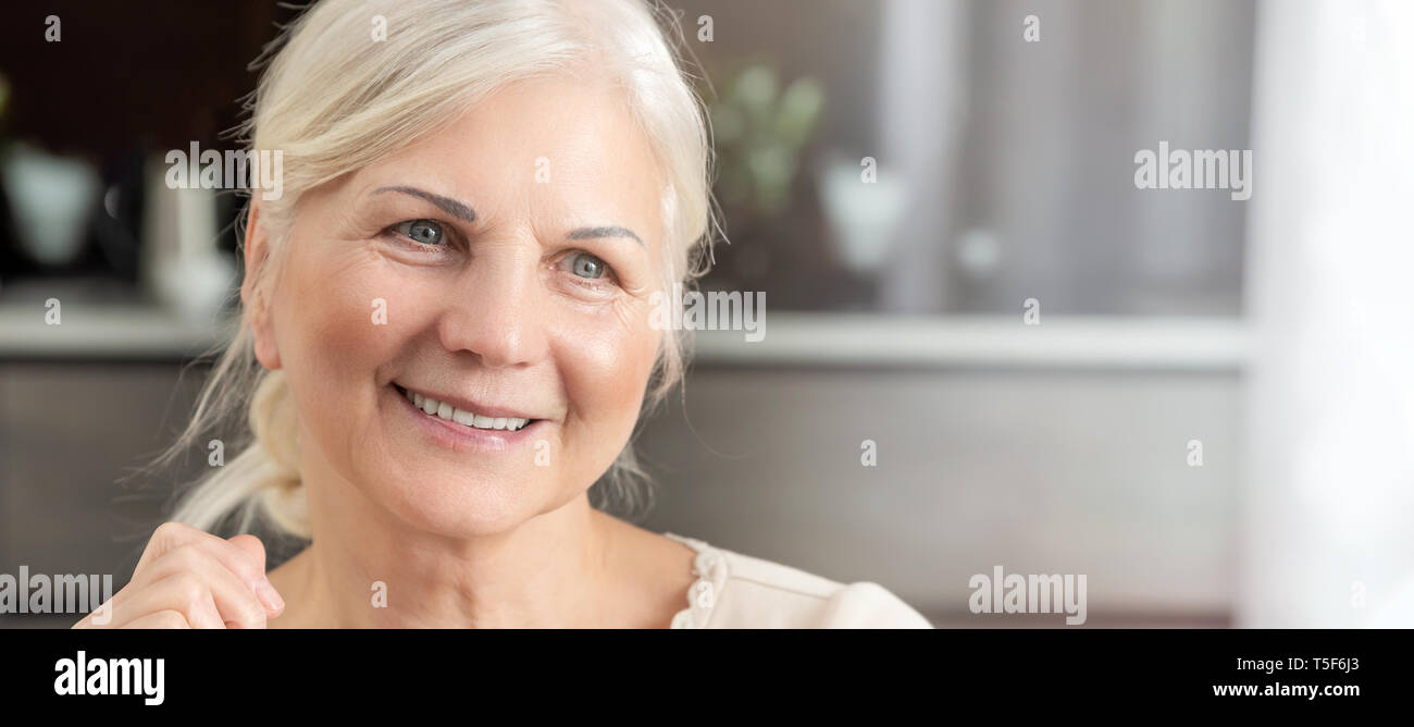 Cheerful senior woman portrait. Pensioner woman sits at home and looks at the window. Concept of a happy retirement Stock Photo