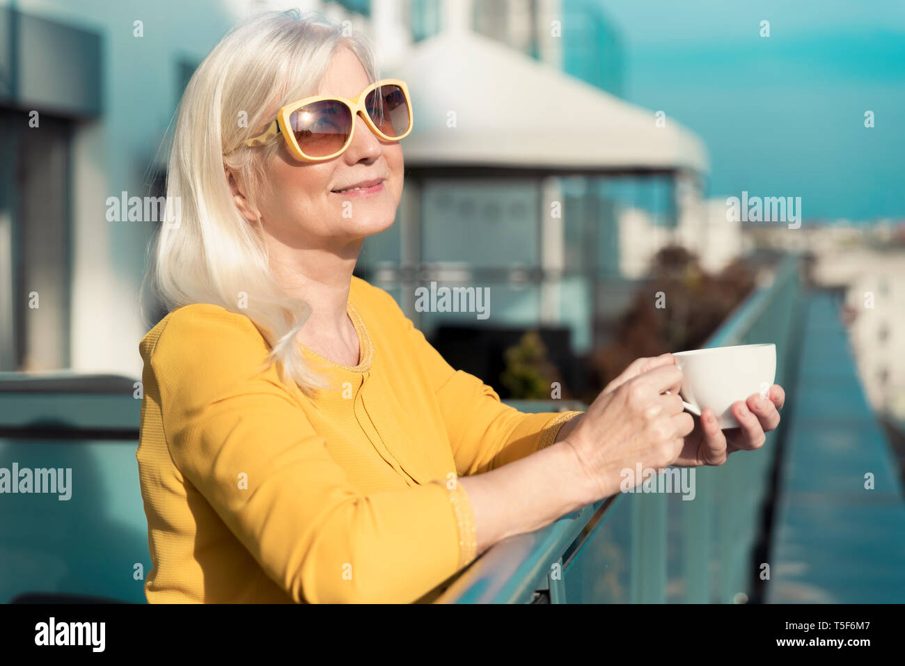 Cheerful, elderly woman enjoying sunny day on balcony. Senior people activity on retirement concept Stock Photo
