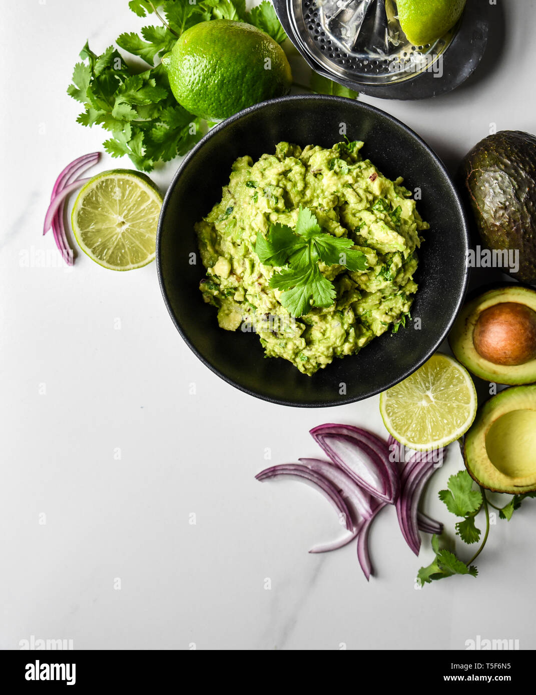 Close up of bowl of guacamole and it's ingredients on a white counter. Stock Photo