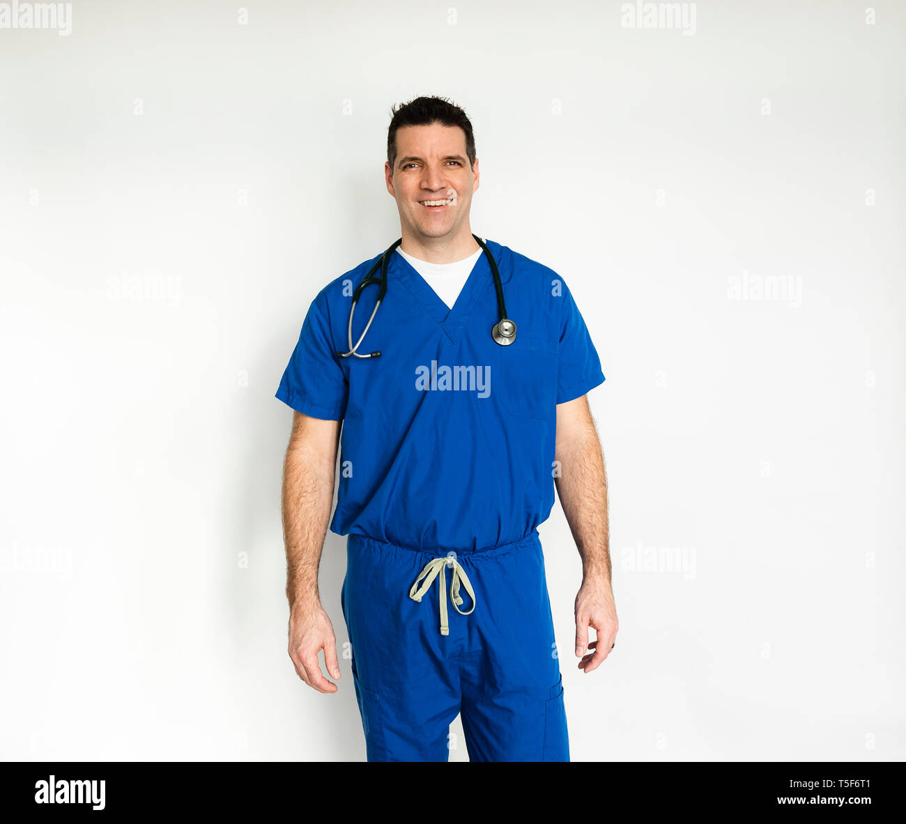 Medical doctor in surgical scrubs standing against a white backdrop. Stock Photo