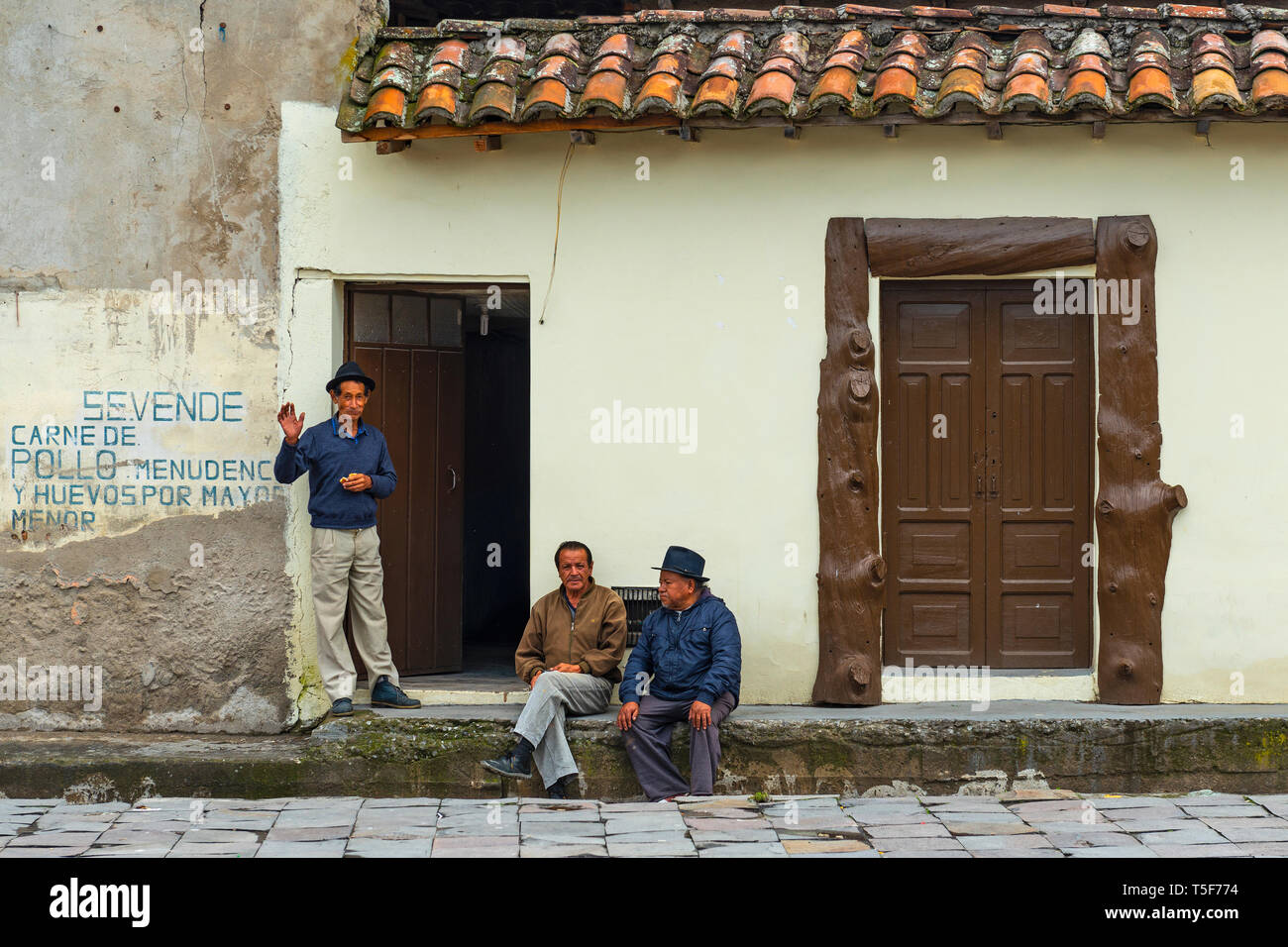 Three senior men talking in front of a house facade in the city of Otavalo, Ecuador. Otavalo is famous for its indigenous textile or poncho market. Stock Photo