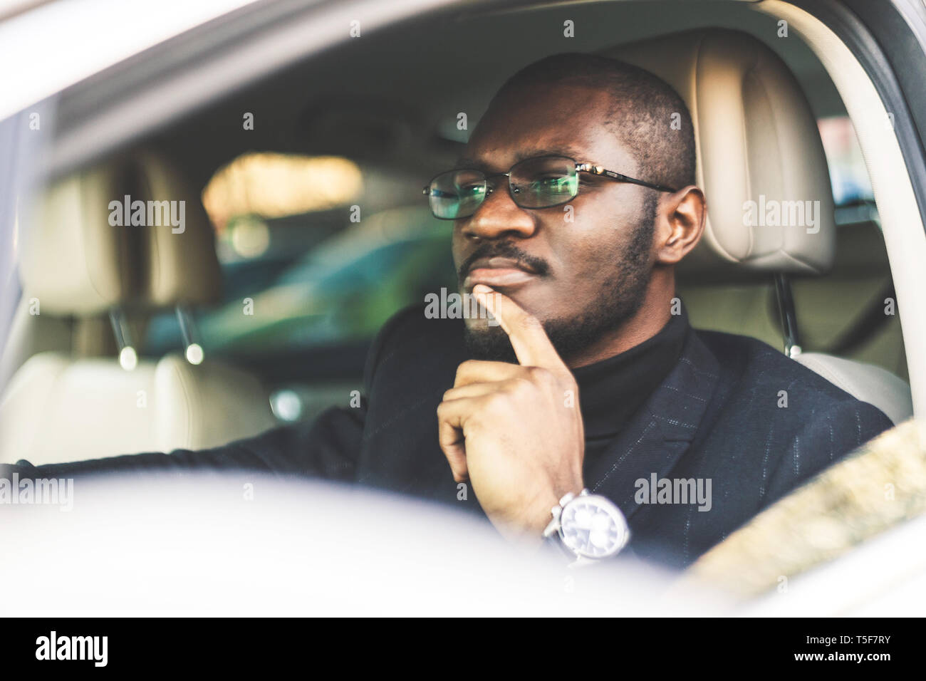 A young businessman in a suit sits at the wheel of a expensive car. Stock Photo