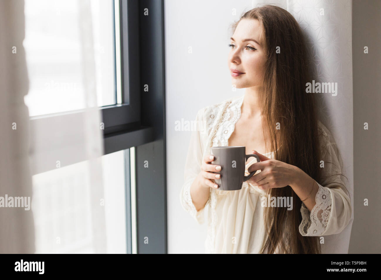 Девушка с кофе в руках у окна
