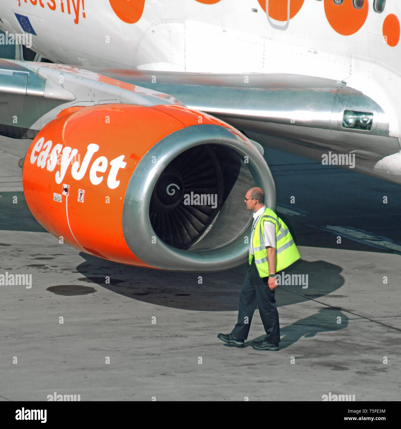 Aviation worker man in high vis jacket at work beside easyJet passenger airplane jet engine nacelle pod on tarmac at Stansted Airport Essex England UK Stock Photo