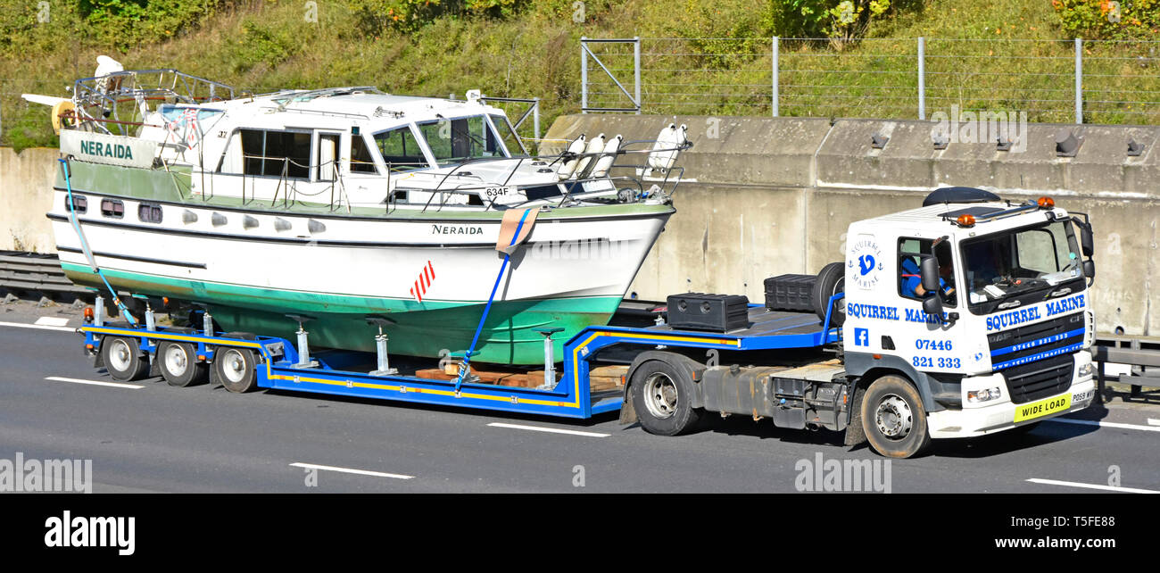 Haulage contractor business with hgv lorry truck & low loader articulated trailer transporting a wide load cabin cruiser boat driving on UK motorway Stock Photo