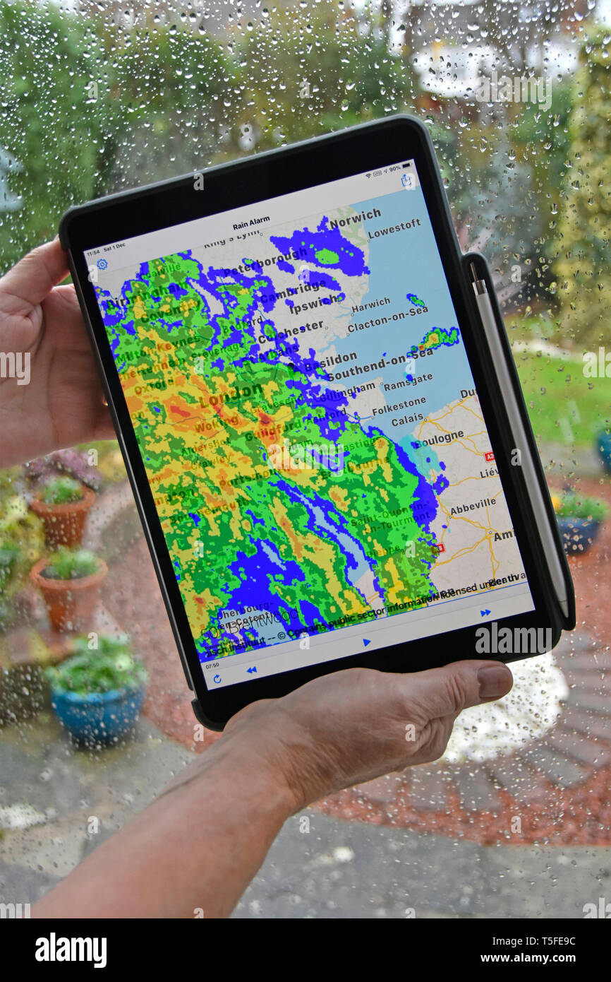 Real time colour radar data superimposing rainfall on local map wet weather on home window hands holding Apple ipad pro tablet rain alarm app Essex UK Stock Photo