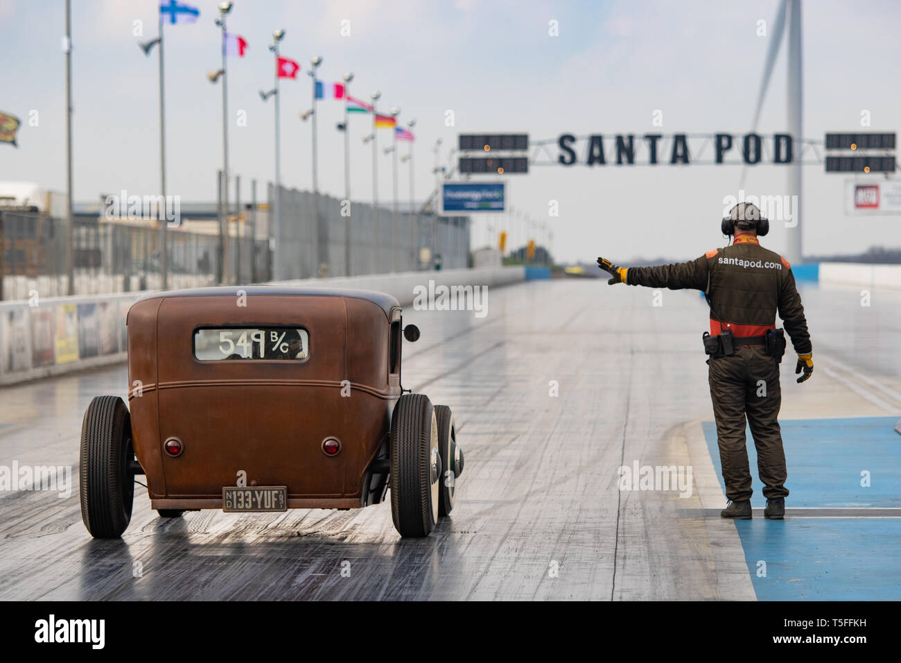 A marshal makes a vintage hot rod car wait in the staging area of the drag strip during the VHRA Vintage Nationals, Santa Pod Raceway Stock Photo