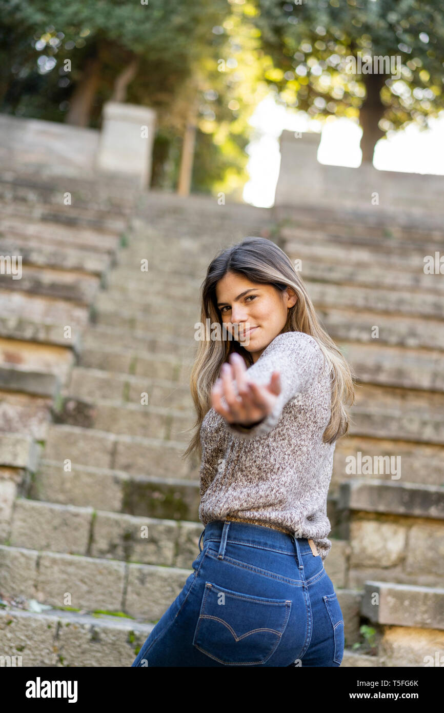 Portrait of a young woman on stairs reaching out her hand Stock Photo