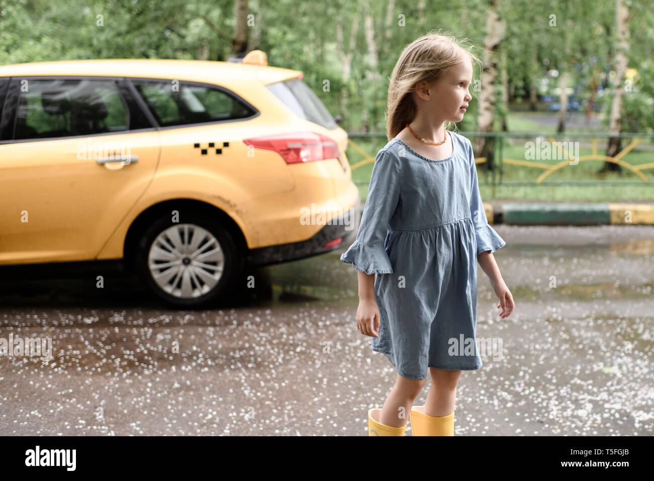 Girl wearing blue dress and vrossing road, yellow car in the background Stock Photo
