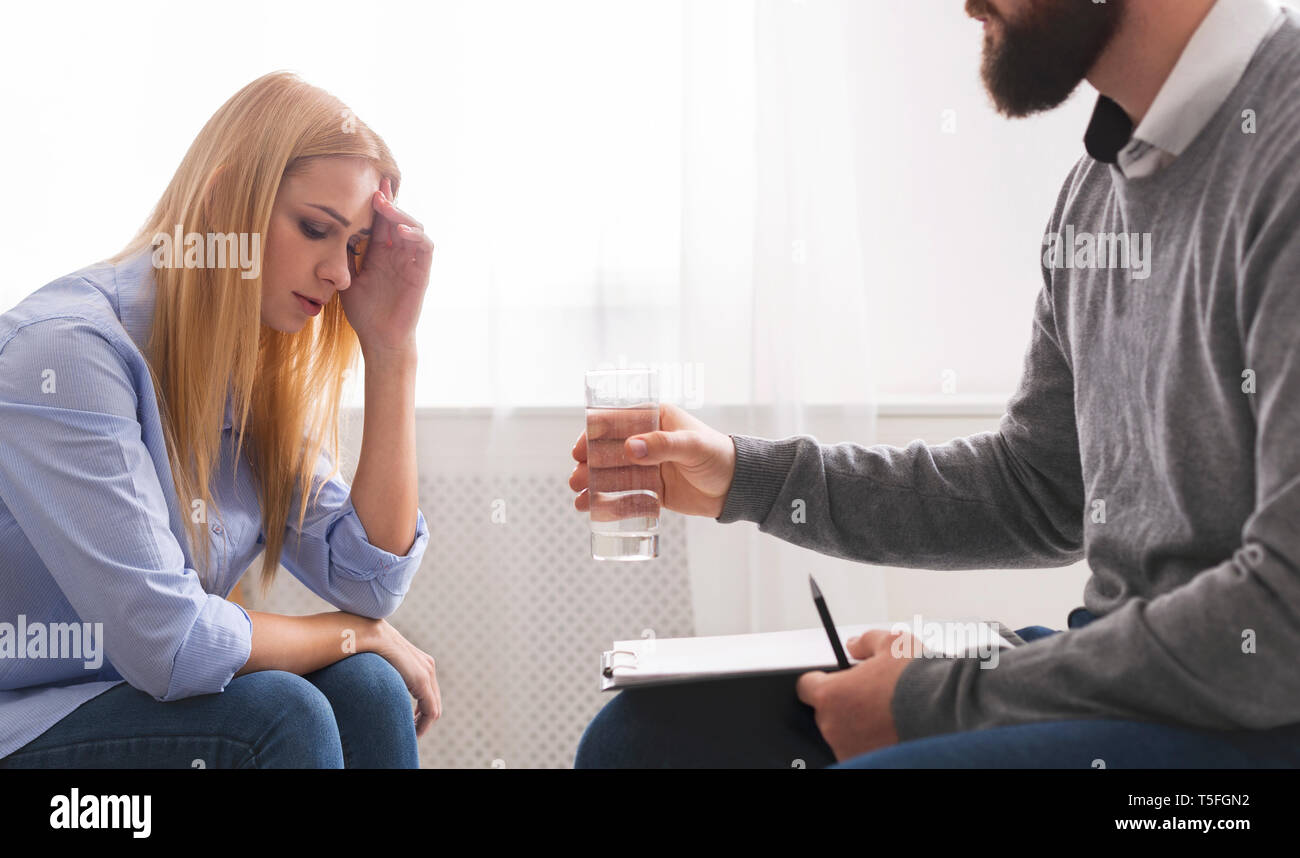 Psychotherapist offering glass of water to upset crying female patient Stock Photo